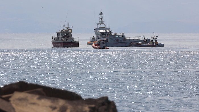 Emergency services work at the scene of a sailboat that capsized on August 19, 2024. Boats are piled up in the sea.