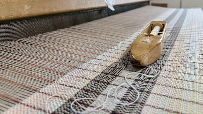 Une navette de bois repose sur une nappe en cours de création sur un métier à tisser.