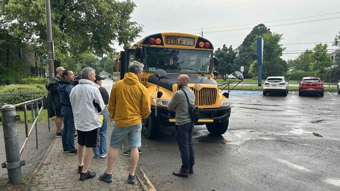 Des personnes font la file pour monter à bord d'un autobus scolaire. 