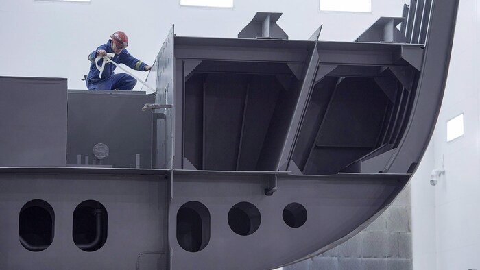 Une image montre un employé du chantier naval Irving à Halifax qui travaille sur une section d'un navire extracôtier et de l'Arctique devant être livré à la Marine royale canadienne