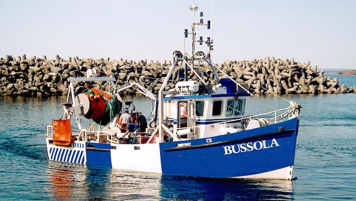 Trois personnes s'affairent sur le pont d'un bateau dans une baie.