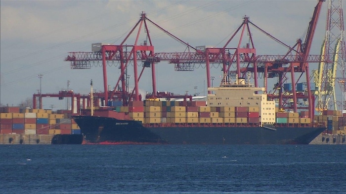 Un navire porte-conteneurs dans le port de Montréal, avec des conteneurs sur le quai