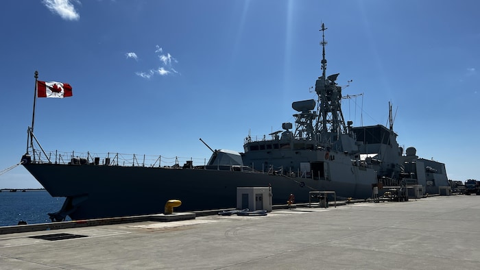 A warship flying the Canadian flag is docked in the port.