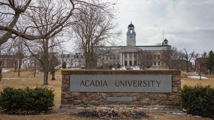 L'enseigne en pierre de l'université devant un édifice bâti au 19e siècle, survolé par une nuée d'oiseaux.