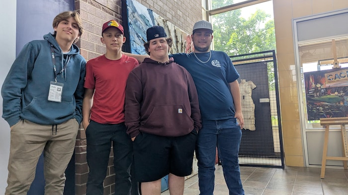 Quatre jeunes posent devant des œuvres d'art.