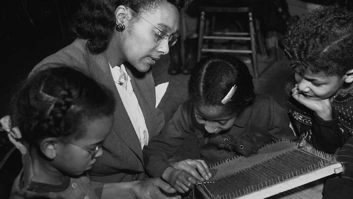 Des enfants tissent à l'aiguille avec l'aide d'une éducatrice au Negro Community Centre.