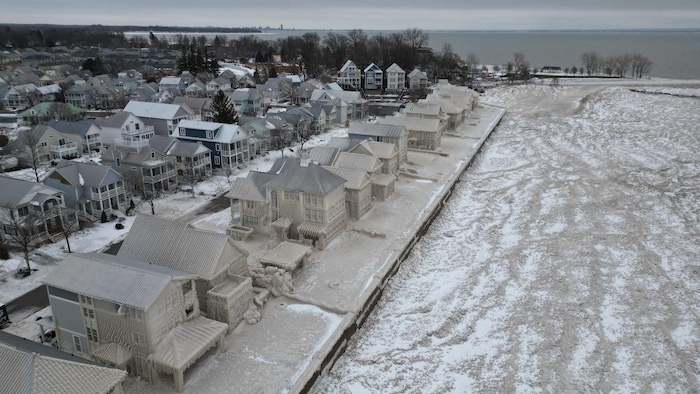 Un rang de maisons recouvertes de neige devant un lac.