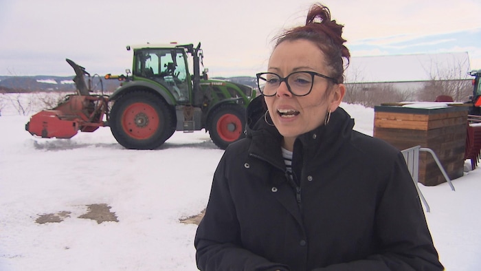 Une femme parle devant un tracteur de déneigement.