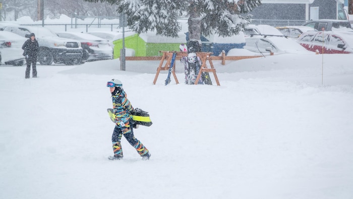 Un jeune tient sa planche à neige devant le stationnement rempli du Mont-Castor.
