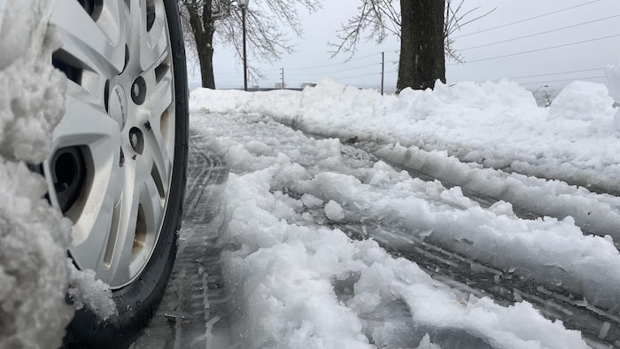 Un pneu à neige de voiture roule sur une route couverte de gadoue.