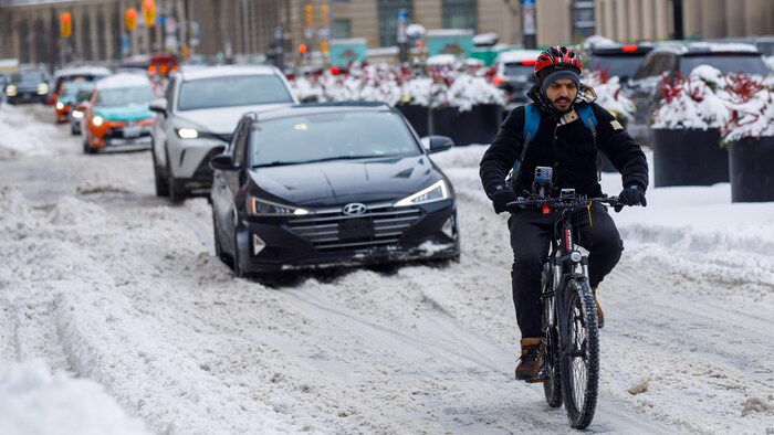 Un cycliste roule dans la neige à Toronto devant des voitures le 13 février 2025.