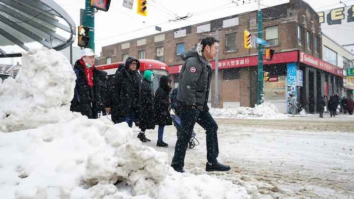 Des gens traversent une rue enneigée devant un tramway.