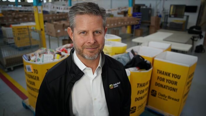 Neil Hetherington sourit à la caméra devant des boîtes remplies de dons.
