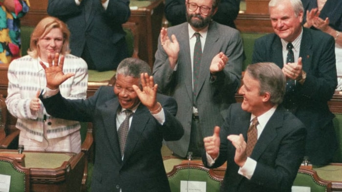 الزعيم الجنوب إفريقي نيلسون مانديلا محيياً أعضاء البرلمان الكندي في أوتاوا في 18 حزيران (يونيو) 1990 على وقع تصفيقهم، وإلى جانبه رئيس الحكومة الكندية برايان مالروني.