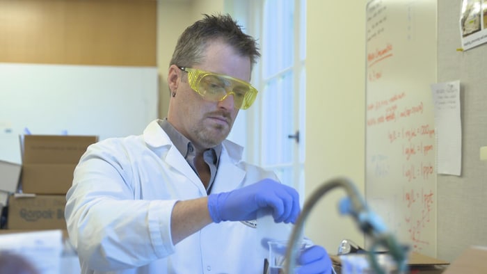 Il collecte un échantillon d'eau dans son laboratoire.