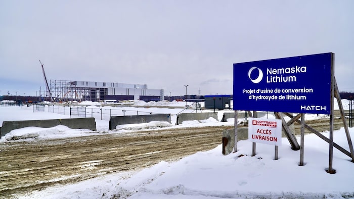 Une pancarte sur laquelle on peut lire : Nemaska Lithium projet d'usine de conversion d'hydroxyde de lithium et on voit au loin une bâtisse en construction.