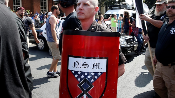 Un hombre lleva un escudo rojo con la insignia del Movimiento Nacionalista Socialista