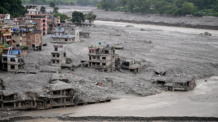 Des maisons lourdement endommagées sont partiellement submergées dans la boue près d'un cours d'eau.