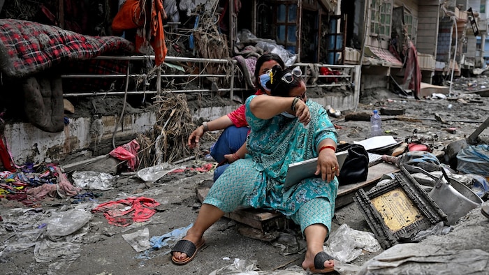 Une femme passe son bras sur son visage, semblant essuyer des larmes, assise au milieu d'une rue jonchée d'objets divers laissés par le passage de la crue.