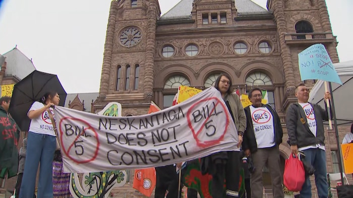 Des manifestants tiennent une banderole qui dit « Neskantaga ne consent pas » devant Queen's Park.