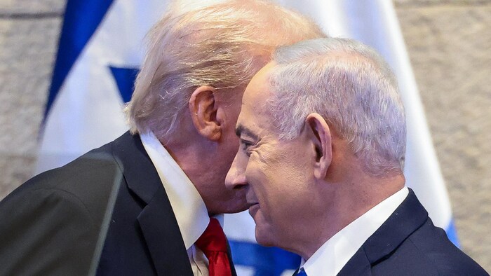 Donald Trump parle à l'oreille de Benyamin Nétanyahou devant un drapeau d'Israël.