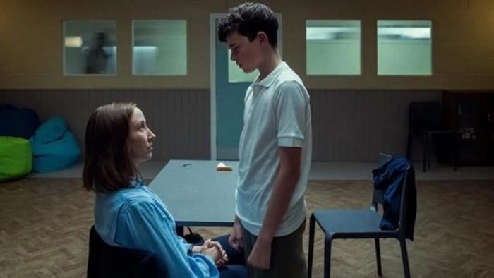 Un teen  debout regarde fixement une femme assise.