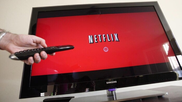 Une main tient une télécommande pointée vers un téléviseur affichant le logo de Netflix.