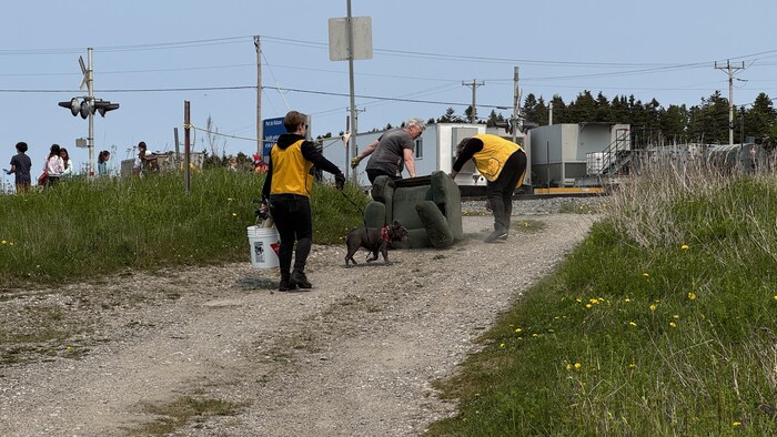 Des personnes déplacent un meuble et une autre porte un seau.