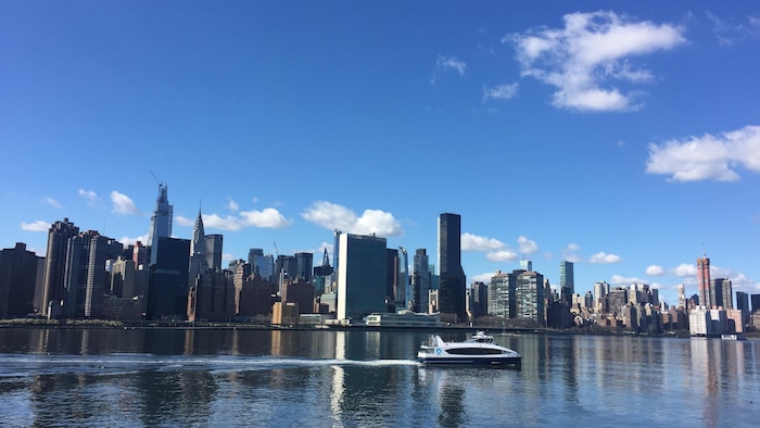 Un petit bateau circule devant la silhouette des gratte-ciel de New York.