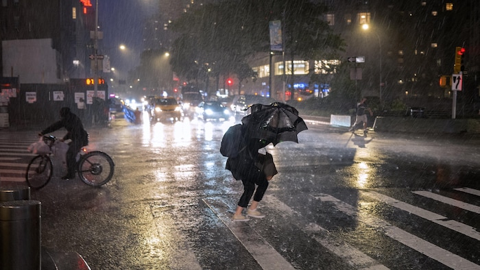 Une femme sous son parapluie traverse une rue de New York alors qu'un torrent de pluie s'abat sur la ville.