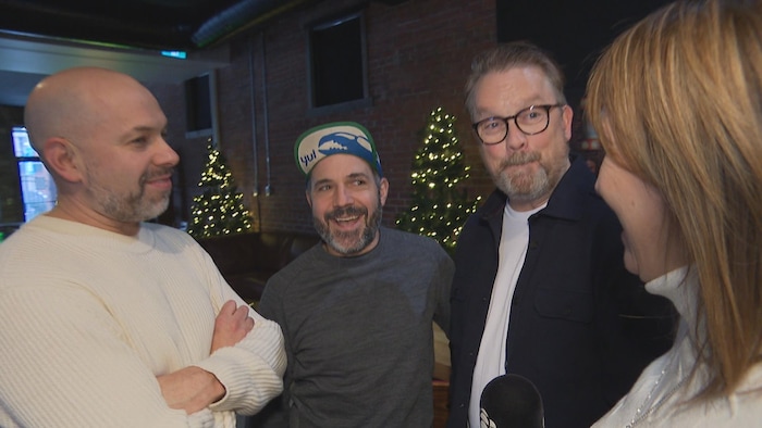 Trois hommes en entrevue avec une journaliste, des sapins de Noël derrière eux.