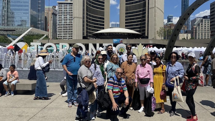 Des nouveaux arrivants de Toronto posent devant le nom emblématique de la métropole canadienne à la place Nathan Phillips.