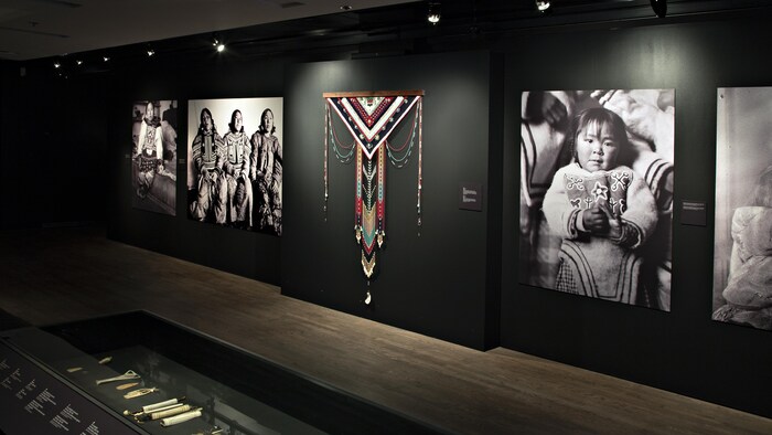 L'œuvre Piqutiapiit, faite de tissus, de cuir, de bois et de perles colorées, avec des portraits de femmes inuit autour.