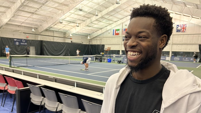 Le joueur de tennis rit aux éclats. Derrière lui, un match de tennis se dispute.