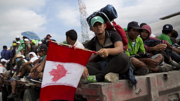 Honduran migrant Fernando Najar Guillen, 22, carries a handmade Canadian flag as he rides on the back of a flatbed truck with other Central Americans, outside Juchitan, Oaxaca state, Mexico, Thursday, Nov. 1, 2018. Najar said he plans to continue across the entire U.S. and seek work in Canada. (AP Photo/Rebecca Blackwell)