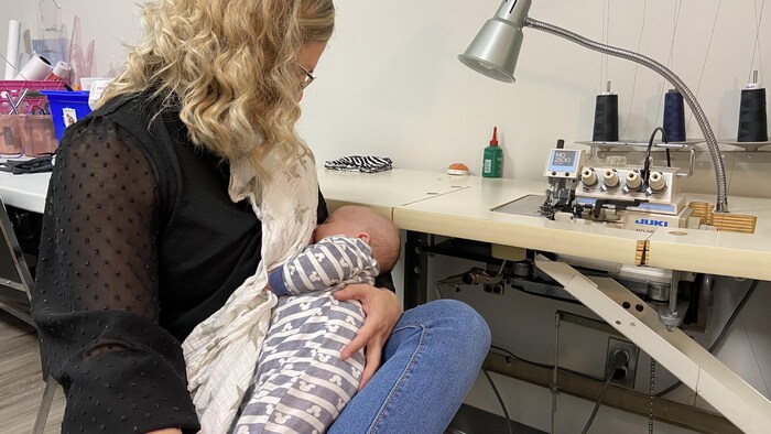 Une femme allaite un bébé devant une machine à coudre.