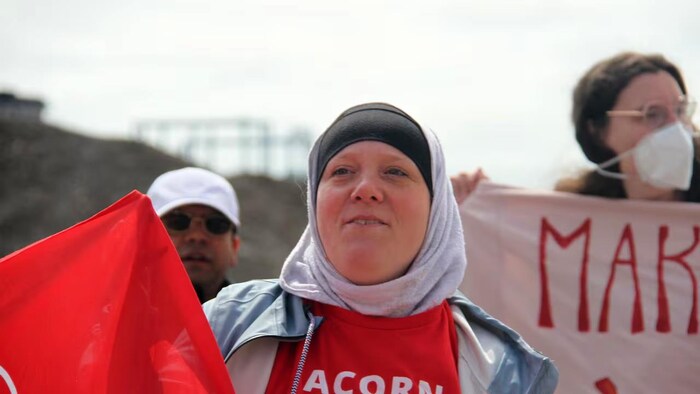 Une femme tient une bannière au milieu d'un groupe de manifestants.