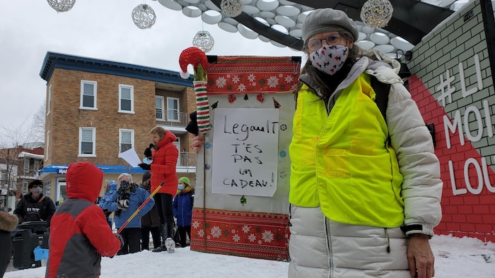 Une femme tient une affiche sur laquelle il est écrit : Legault t'es pas un cadeau.