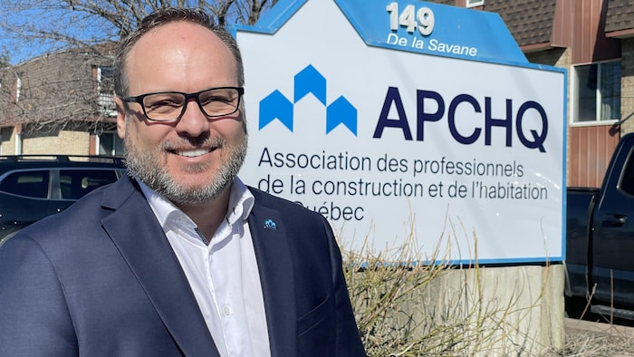 Nicolas Brisson, directeur général de l’APCHQ Outaouais-Abitibi-Témiscamingue, pose devant le logo de l'APCHQ.