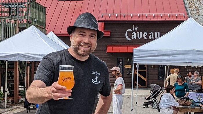 Nicolas Falcimaigne un verre de bierre à la main sur une terrase avec des chapiteaux.