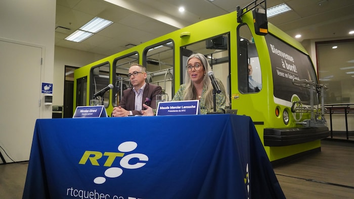 Un homme et une femme en conférence de presse devant une réplique d'un autobus du RTC.