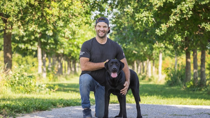 Il pose en souriant aux côtés d'un chien.