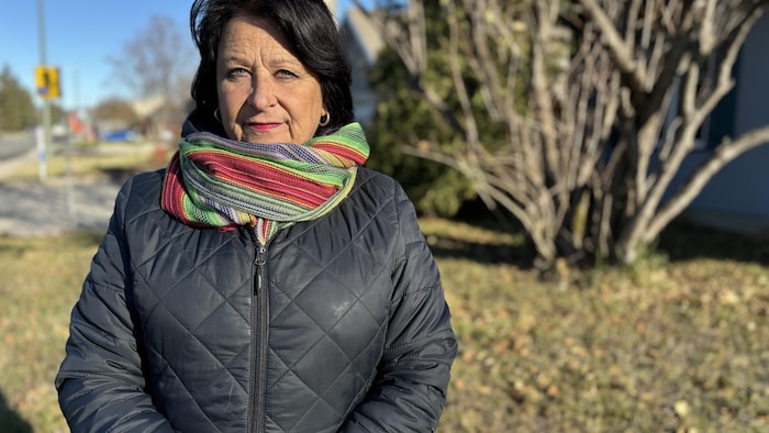 Nicole Dionne devant une rue. Elle porte une écharpe autour du cou.