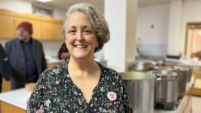 Une femme sourit pour une photo, debout devant des gros chaudrons.