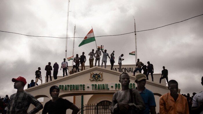 Des manifestants brandissant des drapeaux du Niger sont debout sur un bâtiment.