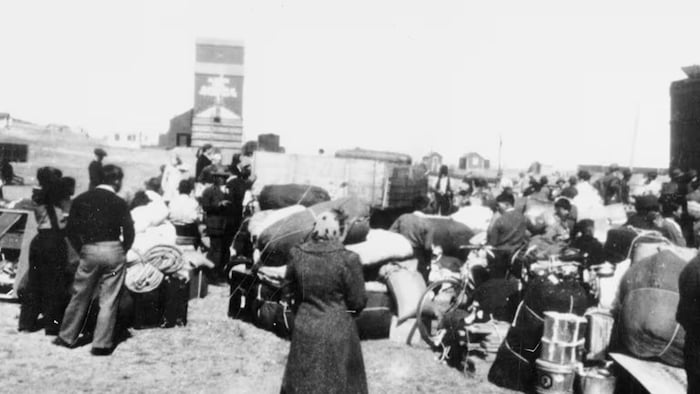 Photo d'archives sur laquelle on voit des personnes prises en photo de dos à l'extérieur, avec des valises.