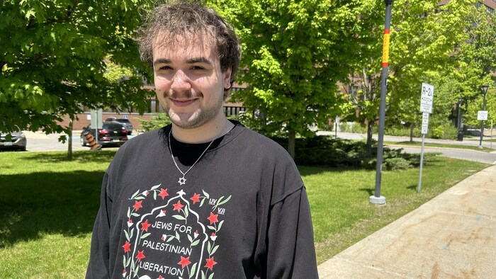 Un homme souriant qui porte un collier avec une étoile de David et un chandail avec écrit: les juifs pour la libération des Palestiniens.


