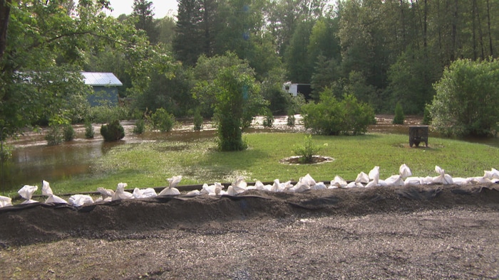 Des sacs de sables sont posés et une tranchée de terre est creusée sur la bordure d'un terrain inondé.