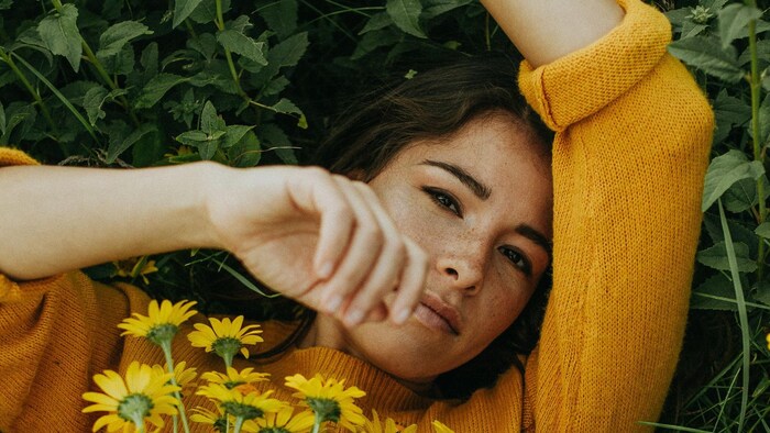 La chanteuse est étendue dans l'herbe, recouverte d'un bouquet de fleurs jaunes. 