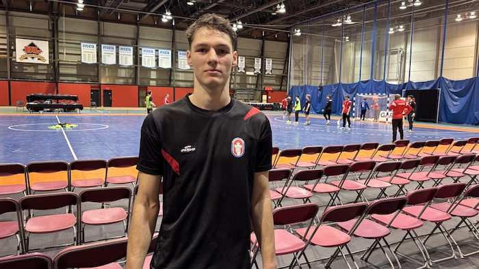 Il pose pour la photo devant un terrain de handball.